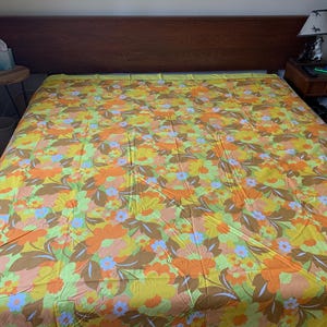Puede incluir: Un edredón floral vintage con un patrón de flores naranjas, amarillas, marrones y azules sobre un fondo verde claro.