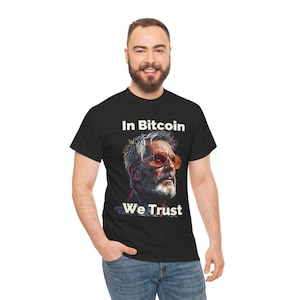 Puede incluir: Camiseta negra con un gráfico blanco de un hombre con gafas de sol y el texto "In Bitcoin We Trust".