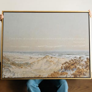 May include: A framed landscape print with a gold frame. The artwork depicts a beach scene with sand dunes, the ocean, and a cloudy sky. The text "Come to me, all you who are weary and burdened, and I will give you rest. Matthew 11:28" is printed on the top.