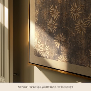 May include: A framed artwork featuring a repeating floral pattern in cream and gold on a dark blue background. The artwork is displayed in a gold frame, creating a sophisticated and elegant aesthetic. The image is well-lit, highlighting the details of the design.