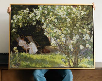 May include: A rectangular framed painting depicting a person in a white outfit sitting in a wooden lounge chair under a large, blooming white rose bush. The scene includes green grass, deep shadows, and a small brown animal resting on the ground.