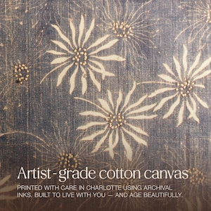 May include: Artist-grade cotton canvas with a repeating floral pattern in cream and tan on a dark blue background. The text reads: "PRINTED WITH CARE IN CHARLOTTE USING ARCHIVAL INKS. BUILT TO LIVE WITH YOU - AND AGE BEAUTIFULLY."