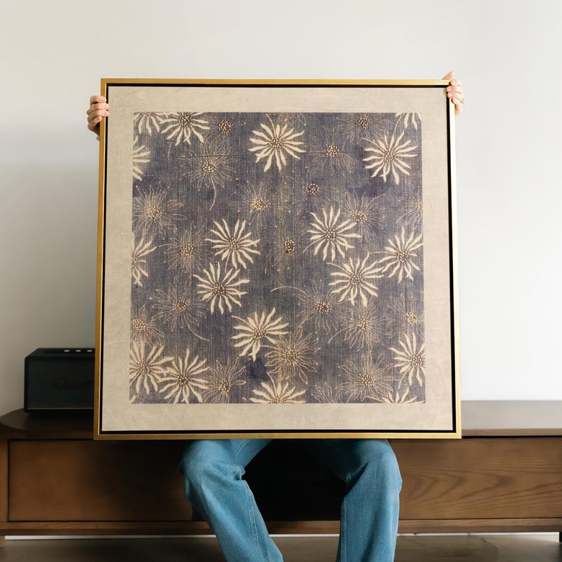 May include: A framed artwork featuring a repeating pattern of stylized, cream-colored floral shapes on a dark blue background. The artwork is encased in a gold-colored frame.
