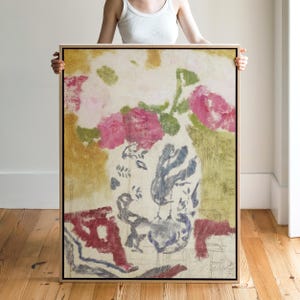 Könnte beinhalten: Abstrakte Blumenmalerei in einem Holzrahmen. Das Kunstwerk zeigt rosa Rosen, grüne Blätter und eine blau-graue Vase vor einem cremefarbenen und gelben Hintergrund. Das Gemälde wird von einer Person gehalten.