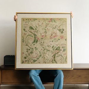 Puede incluir: Una pieza de arte mural cuadrada enmarcada con un fondo verde claro y un patrón repetitivo de pájaros verdes, flores rosas y enredaderas. La obra está encerrada en un marco dorado fino con un borde blanco texturizado alrededor de la impresión.