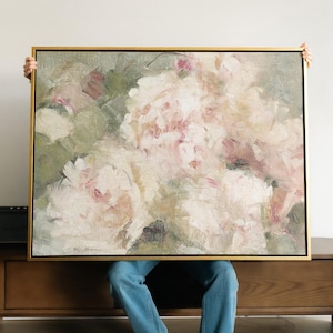 May include: An abstract floral painting in a gold frame. The artwork features a close-up of white and pink flowers with green foliage, rendered with visible brushstrokes. The painting has a soft, textured appearance, with a neutral background.