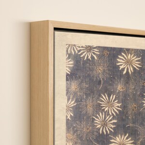 May include: A framed artwork featuring a blue background with a repeating pattern of white, stylized floral designs. The artwork is framed in a light-colored wooden frame, adding a natural touch to the piece.