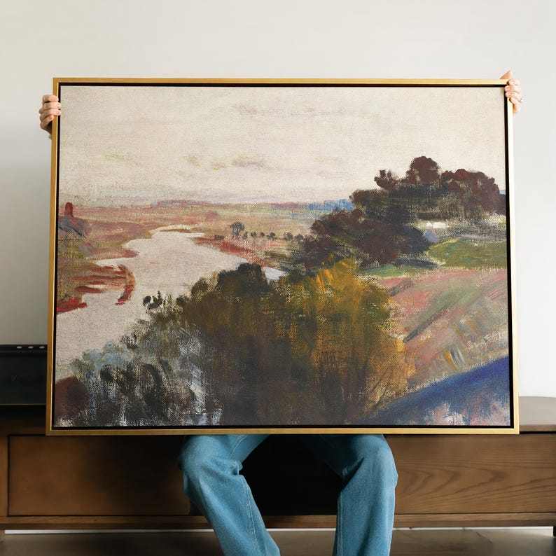 May include: A landscape painting in a gold-coloured frame. The artwork shows a river winding through a valley, with trees and fields in the background. The colour palette includes muted tones of brown, green, and blue.
