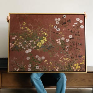 May include: A rectangular wall art piece in a thin gold frame featuring a dark terracotta background with a botanical illustration of various wildflowers, including white pom-pom flowers, yellow clusters, and thin green grasses.