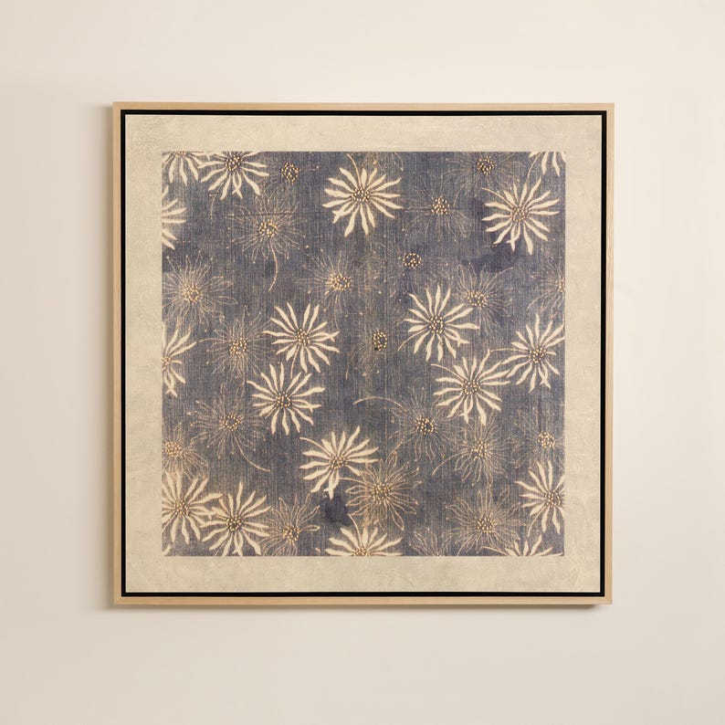 May include: Square framed artwork featuring a blue background with a repeating pattern of white, starburst-like floral designs. The artwork is framed in a light-colored wooden frame with a neutral-toned border.