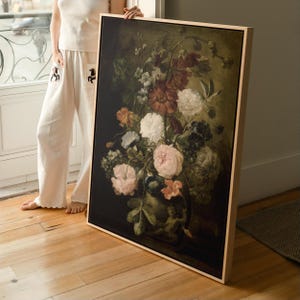 May include: A rectangular framed canvas print featuring a dark, moody floral still life painting. The artwork displays a lush bouquet of white, pink, and deep red flowers with green foliage set against a black background, housed in a light wood frame.