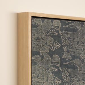 May include: A framed canvas print featuring a detailed pattern of birds and floral elements in a muted beige color against a dark blue background. The artwork is encased in a natural wood frame, adding a touch of rustic elegance.