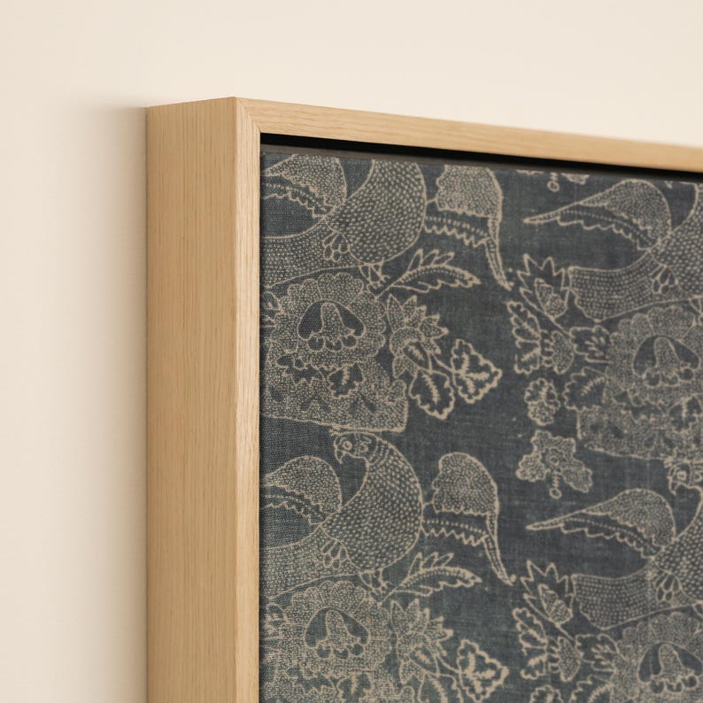 May include: A framed canvas print featuring a detailed pattern of birds and floral elements in a muted beige color against a dark blue background. The artwork is encased in a natural wood frame, adding a touch of rustic elegance.