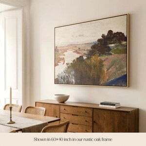 May include: A framed landscape painting, 152 x 102 cm, in a rustic oak frame. The artwork shows a river flowing through a valley, with trees and hills in green, brown, and blue hues. The painting is displayed above a wooden sideboard.