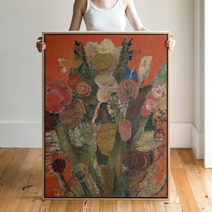 Könnte beinhalten: Gerahmtes Blumenbild mit einer lebendigen Farbpalette. Das Kunstwerk zeigt einen Blumenstrauß in Rot-, Rosa-, Gelb- und Grüntönen vor einem rot-orangen Hintergrund. Das Gemälde wird von einer Person gehalten.