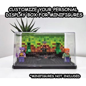 Könnte beinhalten: Eine transparente Plastik-Vitrine mit schwarzem Sockel, die eine grüne und braune Minecraft-Kulisse zeigt. Die Vitrine enthält vier Minifiguren, darunter eine lila gekleidete Figur mit einem Schwert, eine grüne Figur mit einer Spitzhacke und zwei orange gekleidete Figuren. Der Text "Customize Your Personal Display Box For Minifigures" befindet sich oben im Bild, und der Text "*Minifigures Not Included" befindet sich unten.