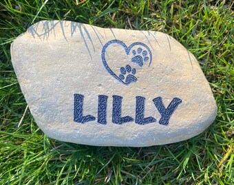 Può includere: Una pietra di colore grigio chiaro con un cuore e impronte di zampe incise su di essa. Il nome "Lilly" è inciso sotto il cuore.