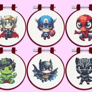 Può includere: Sei telai da ricamo circolari contenenti motivi a punto croce di supereroi in stile chibi. I personaggi includono Thor con un martello, Capitan America con uno scudo, Spider-Man, Hulk, Batman con le ali e Black Panther su tessuto bianco.