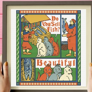 May include: A framed cross-stitch embroidery featuring a comic-style narrative with cats and people. The text reads Do You Sell Fish? and Beautiful. The design uses a palette of red, blue, white, and green, depicting figures at a market stall.