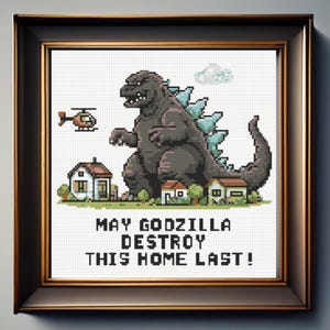 Puede incluir: Un patrón de punto de cruz enmarcado que muestra un Godzilla en arte de píxeles sobre casas pequeñas con un helicóptero en el cielo. El texto debajo dice MAY GODZILLA DESTROY THIS HOME LAST! El diseño utiliza tonos grises, azules y verdes.
