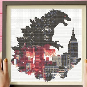 Peut inclure: Un motif de point de croix encadré représentant la silhouette d'un grand monstre gris foncé dominant une ligne d'horizon urbaine. Le design intègre des nuances de rouge, bleu et noir, illustrant un paysage urbain avec un gratte-ciel sur fond blanc.
