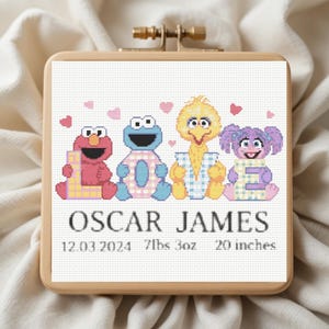 May include: A square embroidery hoop containing a cross-stitch pattern of Elmo, Cookie Monster, Big Bird, and Abby Cadabby forming the word LOVE. Below the characters, the text reads OSCAR JAMES, 12.03.2024, 7lbs 3oz, and 20 inches.