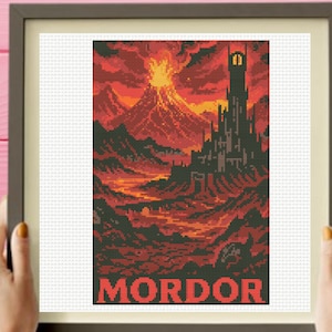May include: A framed cross-stitch embroidery featuring a pixelated landscape of a volcanic mountain erupting with lava, a tall dark tower, and rugged terrain in shades of red, orange, and black, with the word MORDOR printed in red at the bottom.