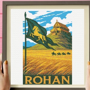 May include: A framed cross-stitch embroidery depicting a landscape with a golden horse on a dark green flag, a wooden building on a hill, and a field of golden wheat. The word ROHAN is stitched in large yellow letters at the bottom of the design.