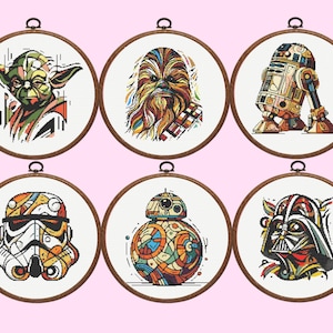 May include: Six circular wooden embroidery hoops containing cross-stitch patterns of science fiction characters. The designs feature colorful, stylized portraits of Yoda, Chewbacca, R2-D2, a Stormtrooper, BB-8, and Darth Vader on white fabric.