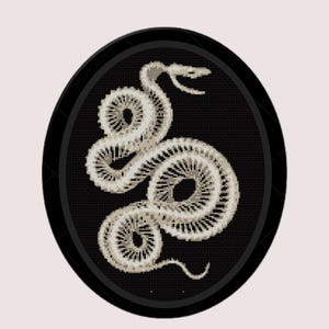 Può includere: Un'immagine ricamata in bianco e nero di uno scheletro di serpente in una cornice circolare.