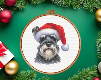 May include: A cross-stitch pattern featuring a Schnauzer dog wearing a red and white Santa hat, displayed within a round wooden embroidery hoop. The dog has grey and black fur with a prominent beard and is centered on a white fabric background.