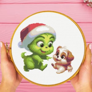 May include: A green Grinch wearing a red and white Santa hat smiles and holds out a hand to a brown and white puppy. The Grinch and puppy are on a white background.