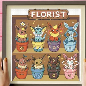 Könnte beinhalten: Kreuzstich-Kunstwerk mit einem "Florist"-Schild über acht bunten Topf-Kreaturen. Die Kreaturen haben verschiedene Farben und Designs, jede in einem einzigartigen Topf. Das Kunstwerk ist in einem braunen Rahmen gerahmt.