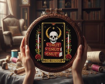 Könnte beinhalten: Ein runder Stickrahmen aus Holz mit einem Kreuzstichmotiv auf schwarzem Stoff. Das Design zeigt einen weißen Totenkopf mit goldenen Hörnern über einem Stapel aus drei roten Büchern mit der Aufschrift SMUT, flankiert von roten Rosen und Kerzen.