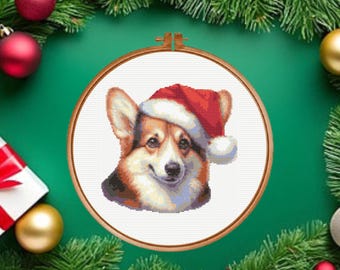 May include: A cross-stitch pattern featuring a portrait of a Corgi dog wearing a red and white Santa hat. The design is displayed within a circular wooden embroidery hoop, showcasing detailed stitching of the dog's face and festive headwear.