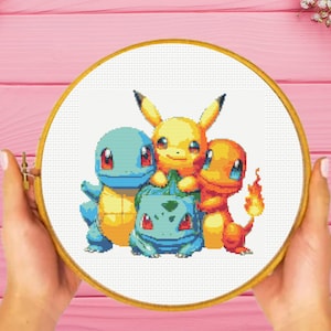 Puede incluir: Un bastidor de bordado circular de madera que contiene un patrón de punto de cruz de cuatro criaturas coloridas. El diseño presenta un personaje azul parecido a una tortuga, un personaje amarillo, una criatura verde y un personaje naranja.
