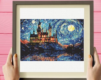 May include: A framed cross-stitch embroidery featuring a castle illuminated by warm yellow lights against a dark blue, swirling night sky with a bright moon and stars. The scene includes a reflection of the castle on the water below in shades of blue.