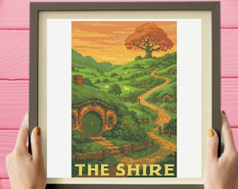 May include: A cross-stitch embroidery pattern in a dark frame depicting a landscape with rolling green hills, a dirt path, a round green door built into a hillside, and a large tree under an orange sunset sky, with the text THE SHIRE at the bottom.