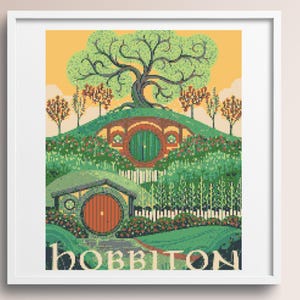 May include: A framed cross-stitch embroidery depicting a landscape with two round doors set into green hills, a large tree, and smaller trees under a yellow sky. The word HOBBITON is stitched in large, light-colored capital letters at the bottom.