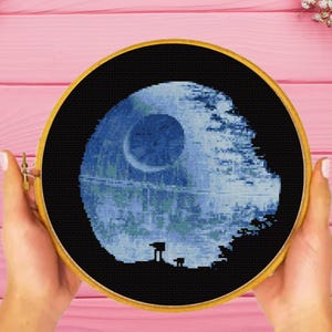 Può includere: Un cerchio da ricamo a punto croce con un'immagine blu e bianca della Morte Nera di Star Wars. La Morte Nera è circondata da uno sfondo nero.