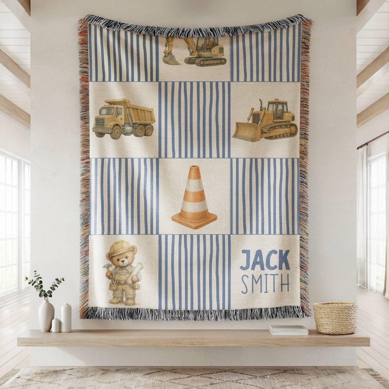 Pu&ograve; includere: Una coperta tessuta con un motivo a griglia di strisce verticali blu e pannelli color crema. Il design include illustrazioni di un escavatore giallo, un camion con cassone ribaltabile, un bulldozer, un cono stradale e un orsacchiotto.