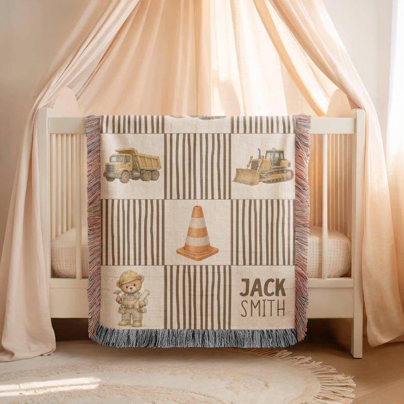 Pu&ograve; includere: Una coperta tessuta con un motivo a griglia con blocchi a righe alternati e illustrazioni di un camion con cassone ribaltabile giallo, un bulldozer giallo, un cono stradale arancione e un orsacchiotto con casco da cantiere, con il nome JACK SMITH.