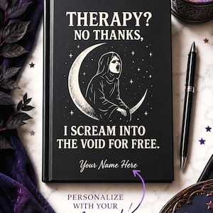 Op de afbeelding: Een zwart notitieboek met harde kaft en een witte afbeelding van een figuur die schreeuwt op een maansikkel, met de tekst THERAPY? NO THANKS, I SCREAM INTO THE VOID FOR FREE. Een paarse pijl wijst naar de plek voor een eigen naam.