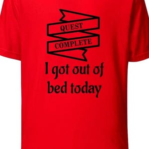 May include: A red t-shirt with the text "QUEST COMPLETE" in a banner design, and the phrase "I got out of bed today" in a playful font. The shirt is a solid red color.