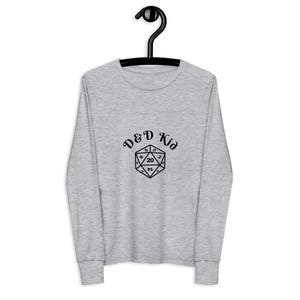May include: A light gray long-sleeve shirt with the text "D&D Kid" above a black twenty-sided die graphic. The shirt is hanging on a black hanger.