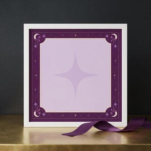 May include: A square framed print featuring a light lavender center with a large four-pointed star. The border is deep purple with small stars, crescent moons, and bows in the corners. A dark purple ribbon lies in front of the white frame.