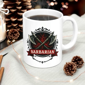 May include: White ceramic mug with a design of crossed axes, a red and black background, and the word "BARBARIAN" on a red banner. The mug is filled with a dark liquid.