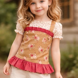 Peut inclure: Une jeune fille porte un haut à imprimé floral avec un volant rouge et un bandeau assorti. Le haut a une base beige avec des fleurs roses et des accents rouges. Elle porte également un short blanc.