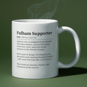 以下が含まれることがあります： 「Fulham Supporter」の文字と定義が書かれた白いセラミックマグ。定義はフラムのサッカークラブのファンについて説明しています。マグカップは湾曲したハンドルを持ち、緑色の背景に配置されています。