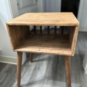 May include: A wooden end table with a shelf and four legs. The table is made of brown wood and has a rustic look.